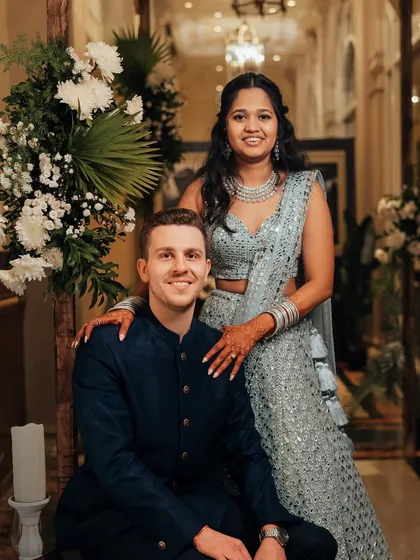 A picture-perfect couple styled for their reception. The bride's hair is styled in gentle waves, complementing her sequined lehenga, while the groom's look is clean and classic in a navy bandhgala.