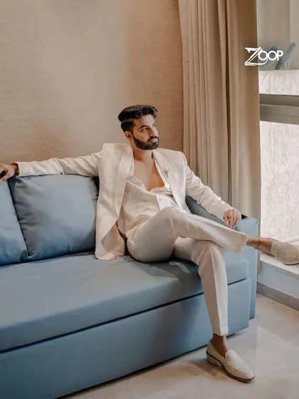 A modern groom relaxing before the ceremony in a sleek, all-white suit. The clean tailoring and comfortable fit make it a perfect choice for a long day of celebrations, from the vows to the reception party.