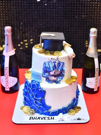 A graduation-themed cake celebrating success. This two-tiered cake is decorated with a graduation cap, a diploma, and edible gold coins.