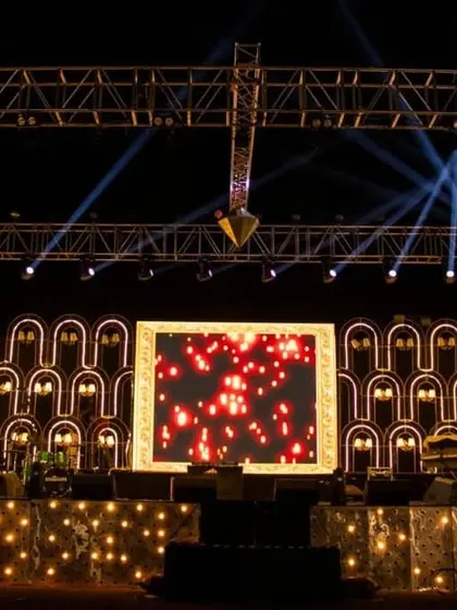 A wide shot of a beautiful sangeet stage design. The backdrop features illuminated art-deco style arches and a central LED screen, creating a versatile and visually stunning set for performances.