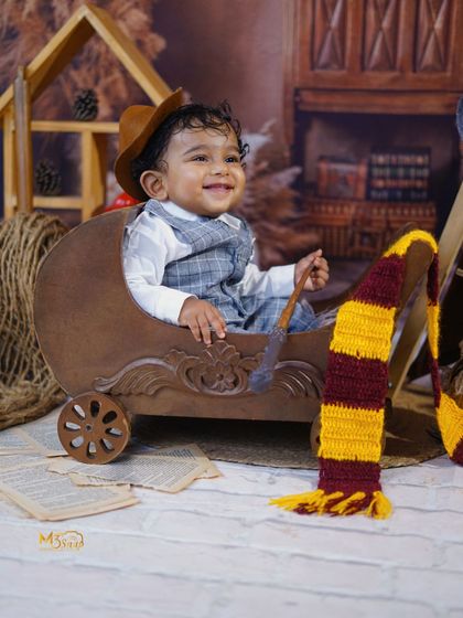 A joyful shot of the baby in a vintage-style wooden car prop, complete with a Harry Potter scarf.