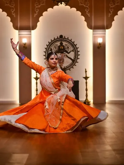 A seated pose in front of a 'Nataraja' idol, a tribute to Lord Shiva, the cosmic dancer. The orange costume radiates energy and devotion.