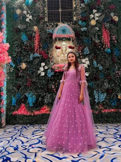 A client posing in a lovely lavender gown with delicate embroidery and sheer cape-like sleeves.
