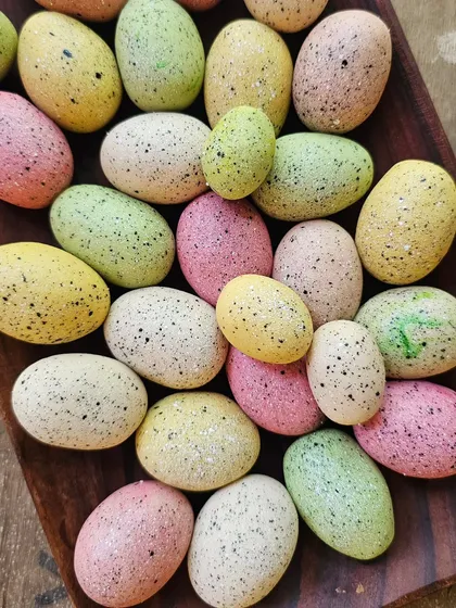 A collection of speckled mini marzipan eggs, colored in soft pastel shades.