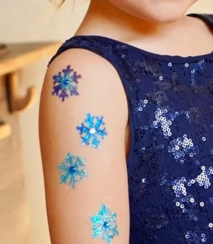 A delicate series of snowflake glitter tattoos on the shoulder. The mix of blue, purple, and silver glitter gives them a lovely icy, wintery feel.