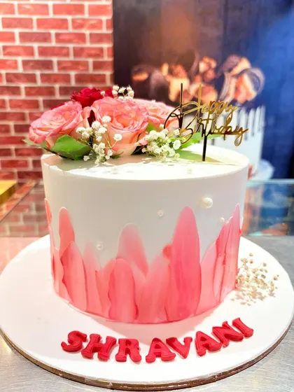 An elegant cake with a pink watercolor effect, topped with fresh roses and baby's breath.