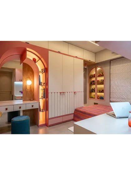 A whimsical and functional bedroom designed with soft pink tones and elegant arches. This view shows the custom vanity with an arched mirror and integrated shelving, alongside a spacious wardrobe.