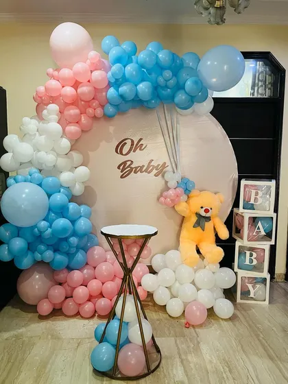 This "Oh Baby" themed decoration is perfect for a baby shower or gender reveal party. It features a large circular backdrop with pink, blue, and white balloons, a cute teddy bear, and "BABY" display boxes. It’s a complete photo corner setup.