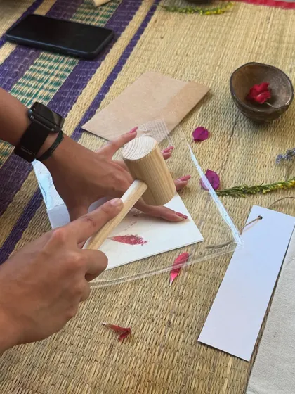 A close-up of the flower pounding technique. Using a wooden mallet, the pigments from the petals are gently transferred onto the paper, creating a soft, watercolor-like effect.