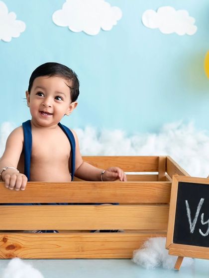 A baby boy sits in a crate next to a small chalkboard with his name, personalizing the photoshoot.