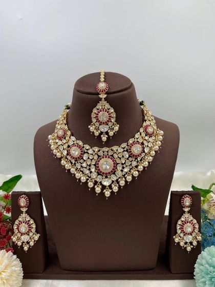 The Zarista Premium Moissanite Necklace set, shown here in both ruby and green variations. This set includes a necklace, maang tikka, and earrings, featuring large central stones surrounded by detailed craftsmanship.