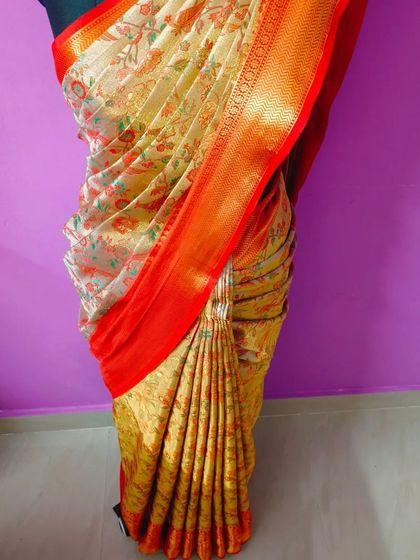A floral saree with a vibrant orange border, draped to perfection. The fluffy pleats add a touch of softness and grace to the overall look.