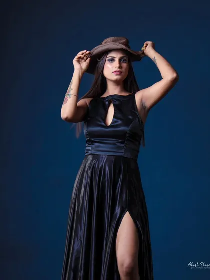 A full-body shot of the model in the black gown against a blue backdrop. The contrast in colors makes the outfit pop.