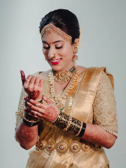 A bride getting ready, wearing a gold Kanchipuram saree. Her custom blouse is fully embroidered with intricate patterns, perfect for her muhurtham look.
