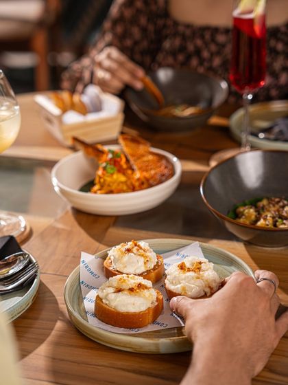 Sharing is at the heart of the Comorin experience. A hand reaches for our signature Cheeni Malai Toast, surrounded by other small plates ready to be passed around.