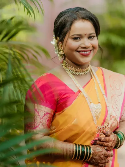 A radiant Maharashtrian bride in a beautiful yellow and pink saree. Her makeup features a bold red lip and a glowing base, creating a timeless and memorable bridal look.