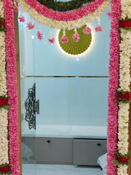 A beautiful floral decoration for a house entrance. The doorway is framed with garlands of pink and white flowers, creating a festive and welcoming atmosphere for a home-based ceremony.