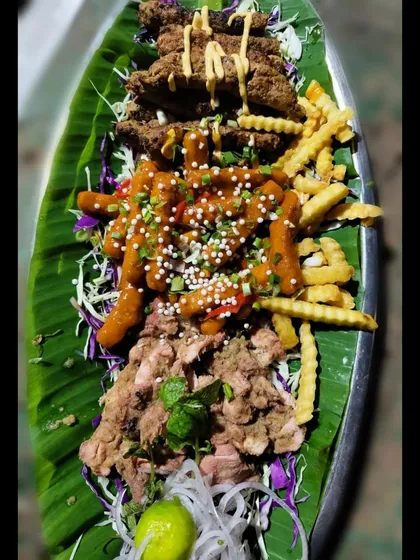 A mixed platter for the true non-veg lover. This features Mutton Seekh, Chicken Chilly Fries, and Chicken Tikka, all beautifully arranged on a banana leaf.