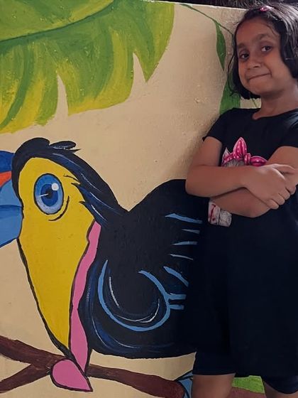 A young admirer posing proudly next to the toucan mural, showing how this art can brighten up a space for the whole family.