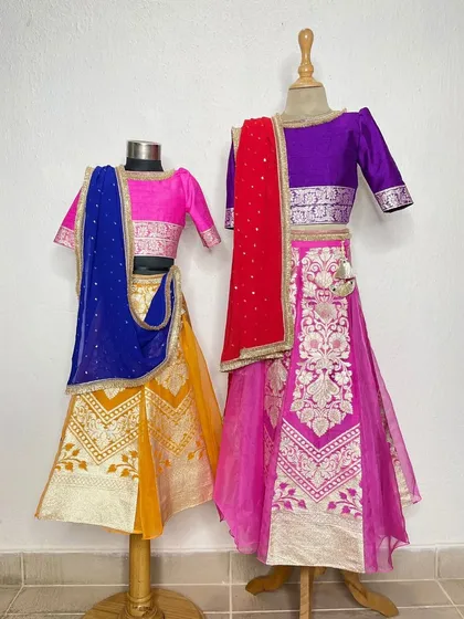 Another view of the sister lehenga sets, showcasing the rich texture of the Banarasi silk and the bright, celebratory colors.