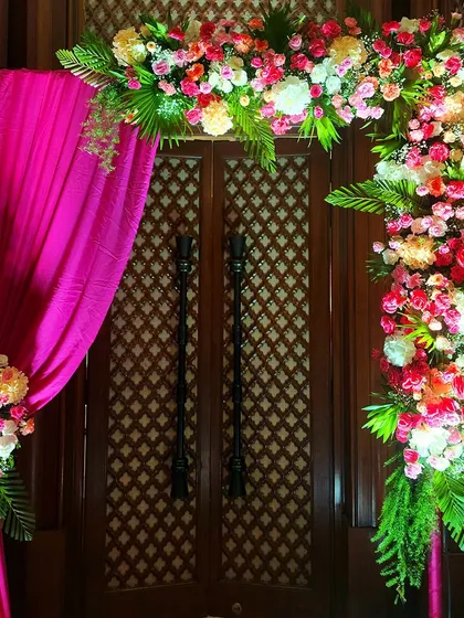 An elegant entrance for a Haldi ceremony, using a bold pink drape and an asymmetrical floral arrangement to create a striking first impression.