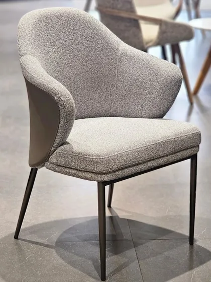 A closer look at the 'LEON' dining chair, showing the texture of the grey fabric and the ergonomic shape of the armrests.