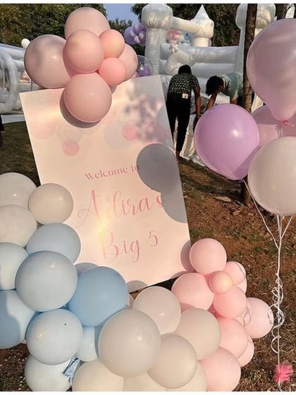 A welcome sign for "Alira's Big 5" surrounded by a soft arrangement of pink, purple, and blue pastel balloons for an outdoor celebration.