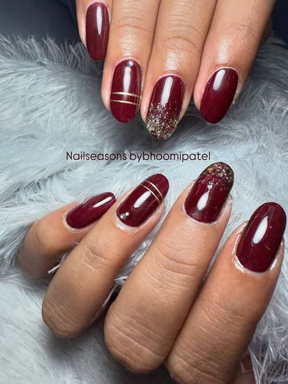 A deep wine-red manicure with gold glitter ombre and simple gold line details.