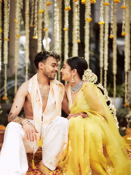 An intimate moment between the couple during their Haldi ceremony. They are dressed in traditional yellow and white, surrounded by strings of jasmine and marigolds.