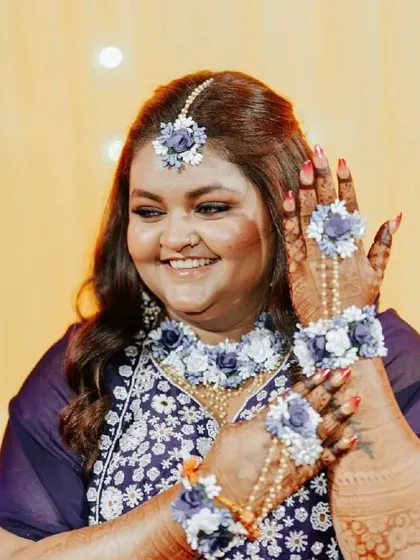 A smiling bride showing off her dark henna, beautifully accessorized with floral jewelry.