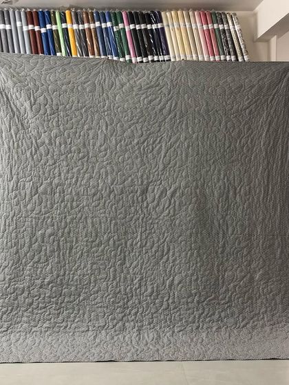 The solid grey backing of the quilt, which highlights the leaf-and-vine quilting pattern.