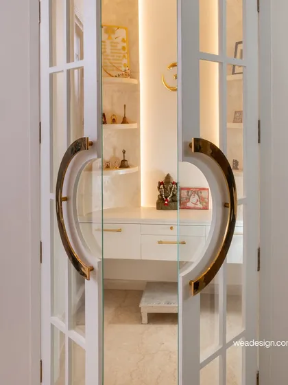 A close-up of the beautifully crafted pooja unit doors with large, curved brass handles, opening up to a brightly lit and serene interior.