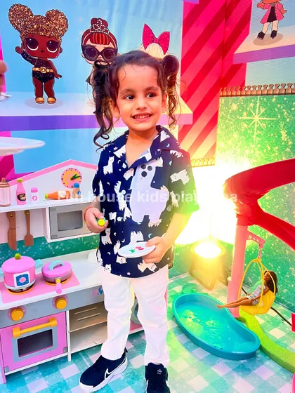 A smiling child posing in front of the play kitchen and Barbie house, surrounded by a world of fun.
