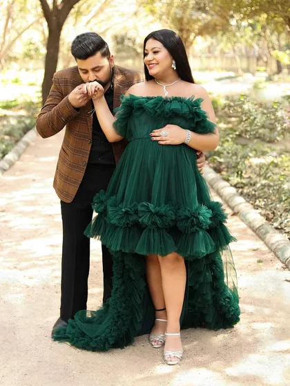 A classic, chivalrous pose with the dad-to-be kissing his partner's hand. Her emerald green high-low gown looks stunning as they take a stroll on a park pathway.