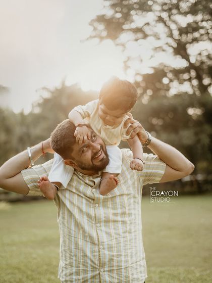 The pure joy of a father with his child on his shoulders, set against a backdrop of golden sunlight. This outdoor family photo is full of laughter and authentic happiness.