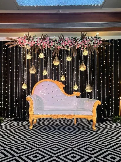 This Sangeet stage combines a black fairy light backdrop with modern geometric flooring. The design is clean and contemporary, with hanging glass terrariums and a floral-topped couch for the couple.