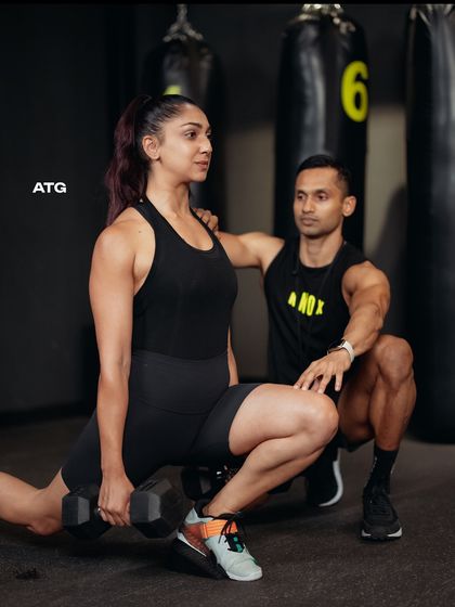 Our coach provides hands-on guidance during a dumbbell lunge, ensuring proper form and knee alignment. This attention to detail is central to our personal training approach.