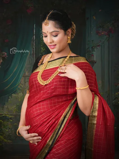 A beautiful studio portrait of a mother-to-be in a traditional red saree, adorned with gold jewelry.