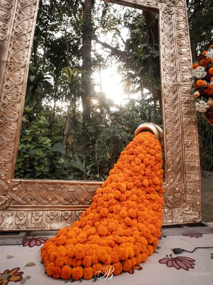 A giant golden frame serves as a photo booth, with a waterfall of marigolds pouring from a traditional pot. This installation combines grand gestures with traditional flowers for a stunning effect.