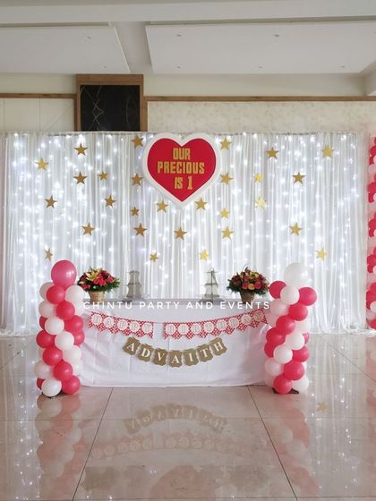 An elegant first birthday decoration with a fairy light curtain backdrop. The simple red and white balloon pillars add a classic touch to the setup.