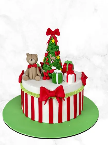 A festive Christmas cake with red and white stripes, topped with a fondant Christmas tree, a teddy bear, and presents.