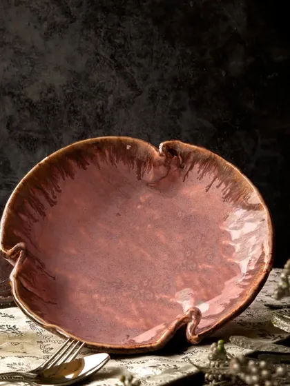 The empty burgundy bowl is the star of this moody, atmospheric shot. The dramatic lighting and dark background highlight its unique, organic shape and rich, textured glaze.