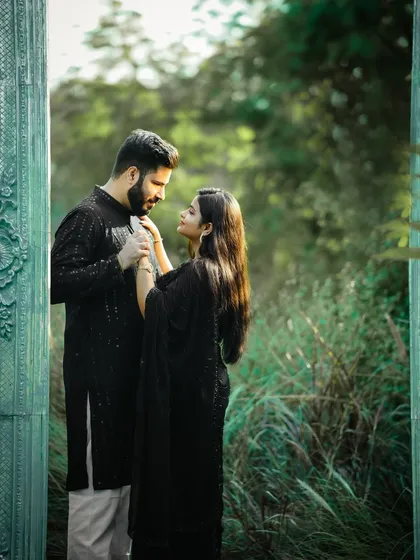 A beautifully composed shot using a doorway to frame the couple. The contrast between their dark outfits and the lush green background makes this pre-wedding photo stand out.