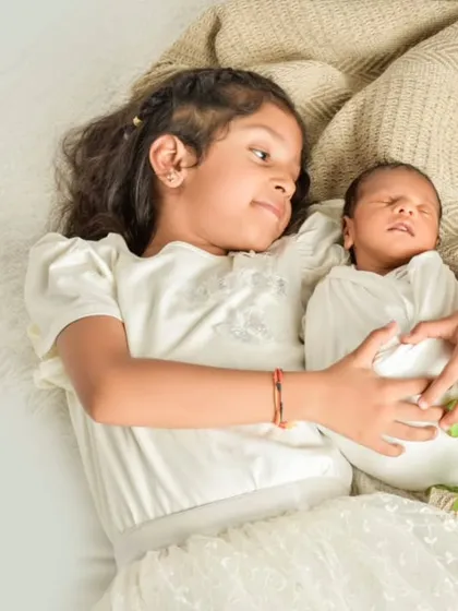 An older sister gently holds her newborn sibling, looking down with a sense of wonder and care. These sibling shots are precious records of a lifelong bond beginning.