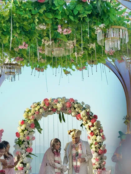 The couple stands under a lush floral arch during their daytime wedding ceremony. The natural light and beautiful setting create a serene and romantic atmosphere.