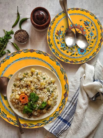 A styled food scene featuring sabudana khichdi served on bright yellow floral plates. This creates a complete lifestyle narrative for the ceramicware.