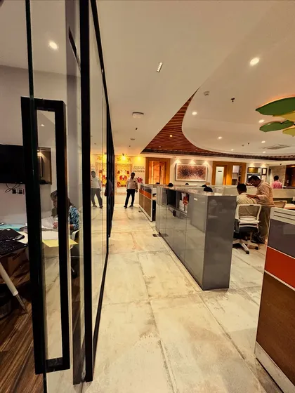 This angle captures the flow and movement within the office. The marble flooring and strategic lighting guide you through the space, leading past the private cabins and towards the collaborative work zones, all under the canopy of the symbolic tree.