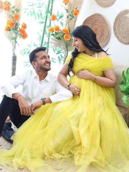 A candid moment of love and laughter between an expecting couple. The bright yellow gown and relaxed boho setting make this a cheerful and heartwarming portrait.