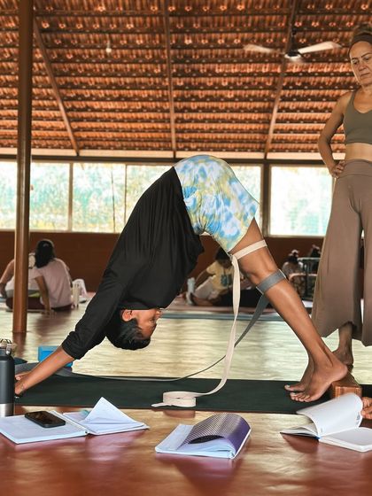In our training, you'll learn to adapt poses for different needs. Here, a student uses a strap around their thighs in Downward-Facing Dog to learn about internal rotation and proper leg engagement.