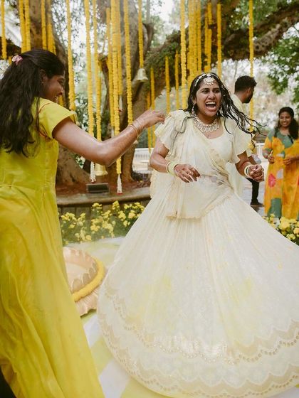 The bride dancing with joy during her Haldi ceremony, surrounded by beautiful yellow floral decor.